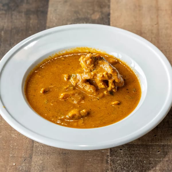 A white bowl filled with a rich, orange-brown curry and pieces of meat.