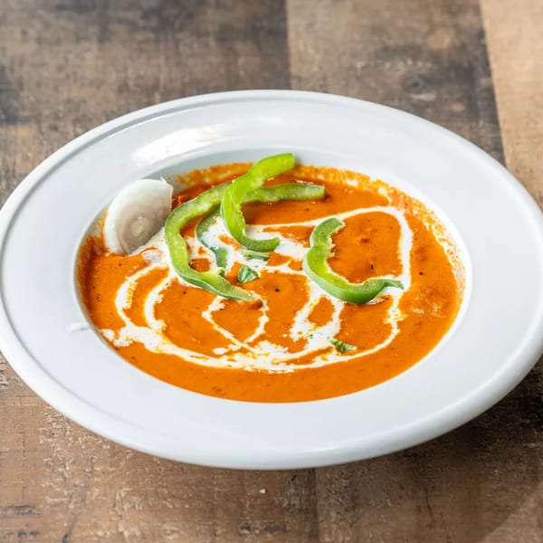 Vibrant orange curry with cream swirls, green bell pepper strips, and a slice of onion in a white bowl.