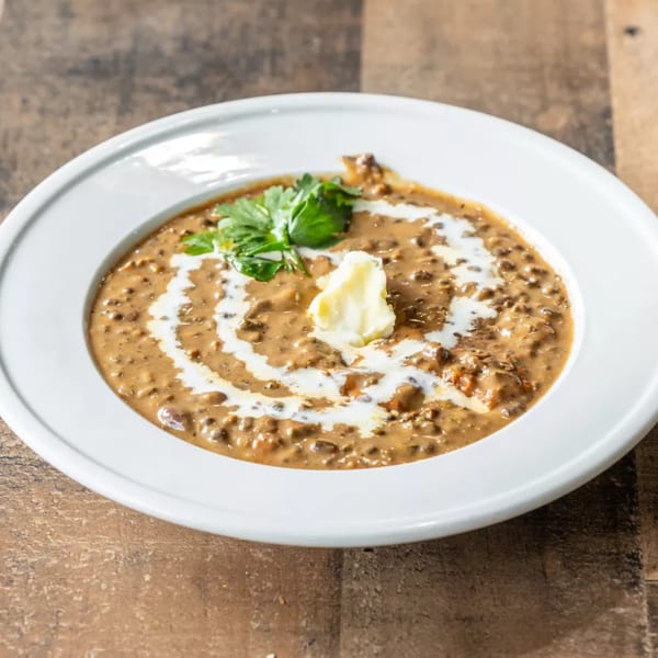A white bowl of creamy brown lentil curry, garnished with a swirl of cream, butter, and cilantro.