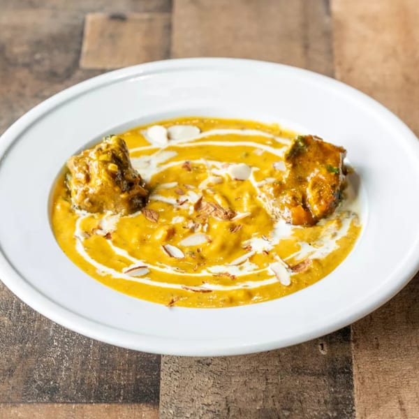 A white bowl filled with a rich yellow curry, garnished with cream swirls and sliced almonds.