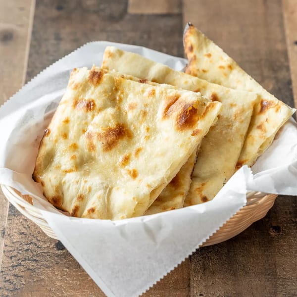 Golden-brown naan bread pieces, served in a white paper-lined basket on a rustic wooden table.
