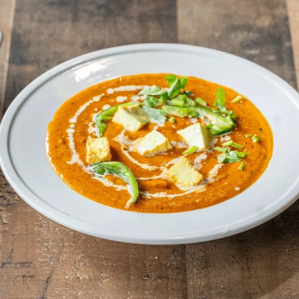 Paneer butter masala with paneer cubes, green peppers, and cream swirls in a white bowl.