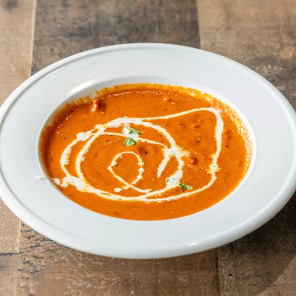 A white bowl filled with creamy orange tomato soup, garnished with a swirl of cream and basil.