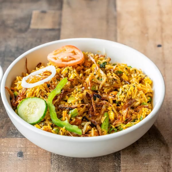 A white bowl filled with yellow biryani rice, topped with fried onions, tomato, cucumber, and green pepper.