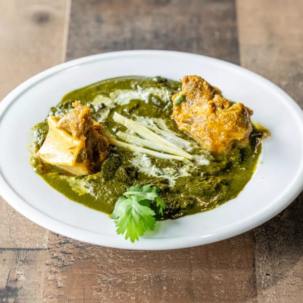 Palak Gosht, a vibrant green spinach curry with tender pieces of lamb, garnished with ginger and cilantro.
