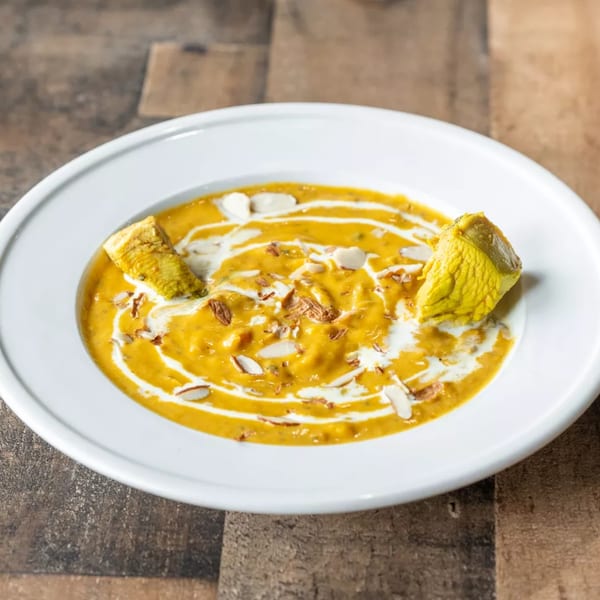 Creamy yellow curry with chicken pieces, drizzled with white sauce and topped with sliced almonds.