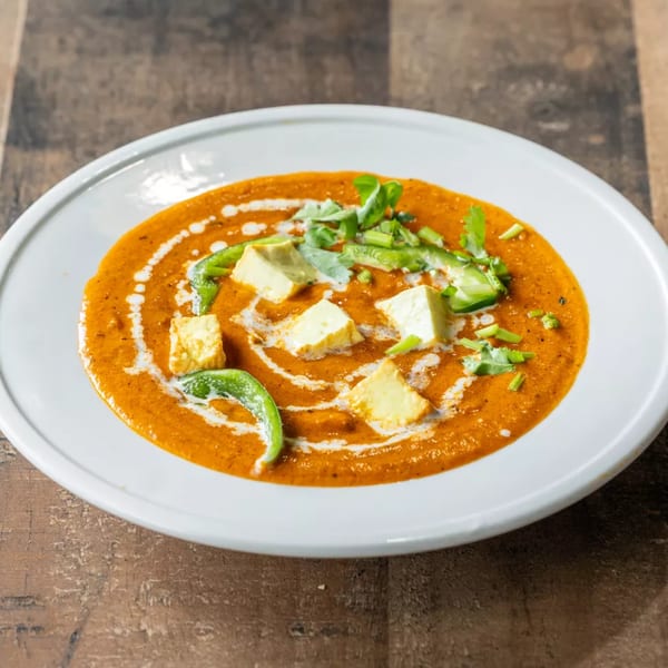 Paneer butter masala with green peppers, cilantro, and cream swirls on a white plate.